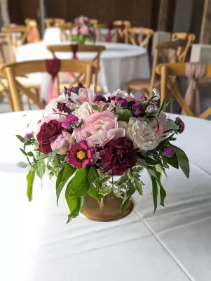 Centre de table romantique organique avec pivoines roses, roses blanches et œillets bordeaux pour mariage.