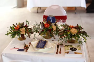 Centre de table bohème avec renoncules orange, œillets crème, feuillage eucalyptus et plumes pour un salon.