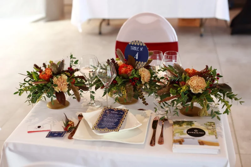 Bohemian table centrepiece with orange ranunculus, cream carnations, eucalyptus foliage and feathers for a lounge area.