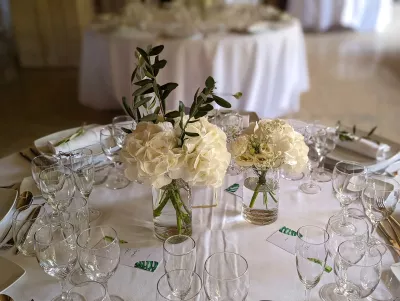 Centre de table rond élégant avec hortensia blanc, renoncules crème et feuillage d'olivier, vase en verre, style classique.