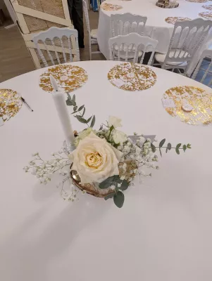 Centre de table rond classique avec une rose crème, du gypsophile, de l'eucalyptus et une bougie, sur une table d'invités.