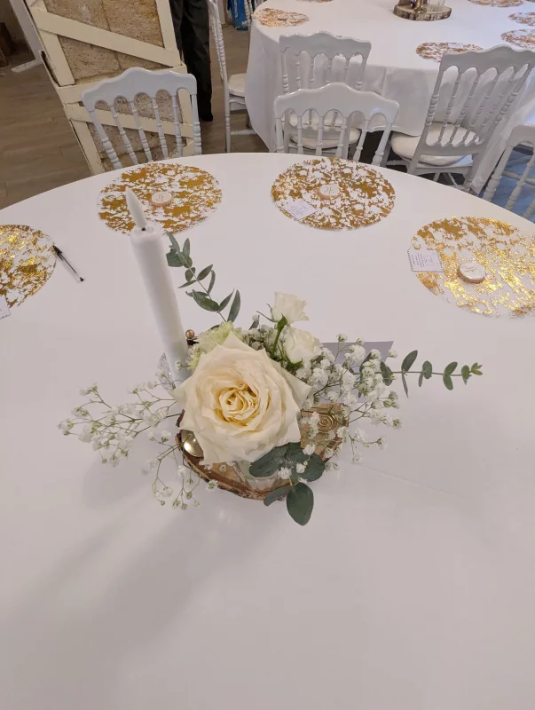 Centre de table rond classique avec une rose crème, du gypsophile, de l'eucalyptus et une bougie, sur une table d'invités.