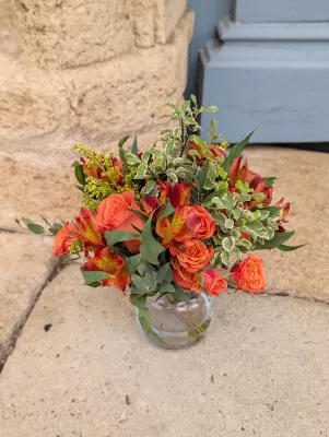 Sophisticated rustic table centrepiece with coral roses, alstroemerias, and various foliage in a glass vase.