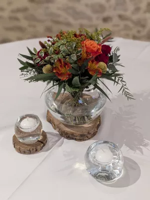 Sophisticated rustic table centrepiece with coral roses, alstroemerias, and red berries, on a wooden base.