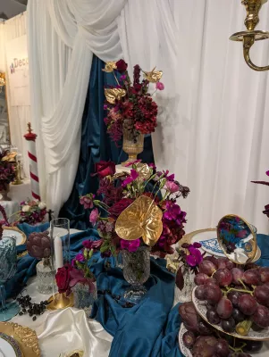 Gros plan sur un centre de table classique avec roses bordeaux, anthuriums dorés et orchidées magenta, agrémenté d'artichauts.
