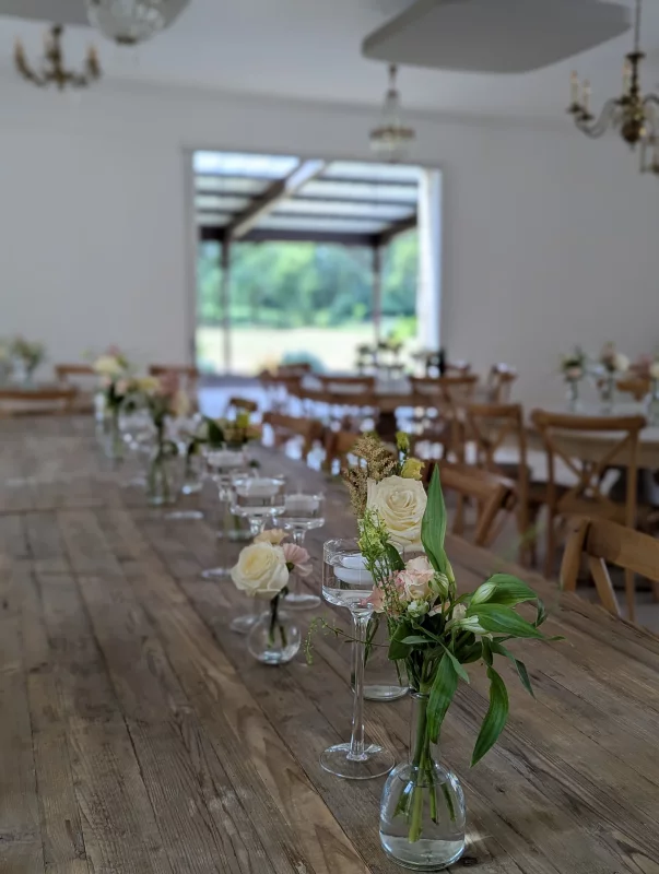 Centre de table champêtre élégant pour mariage, avec roses crème et astilbe rose, feuillage varié sur table en bois.