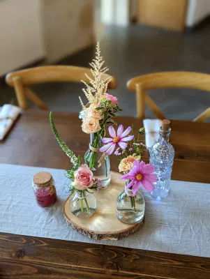 Centre de table champêtre avec roses, cosmos, astilbe dans des vases en verre sur rondin de bois.