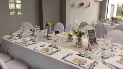 Centres de table champêtres pour un mariage, avec roses blanches, craspedia jaune et gypsophile dans des bocaux décorés.