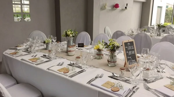 Centres de table champêtres pour un mariage, avec roses blanches, craspedia jaune et gypsophile dans des bocaux décorés.
