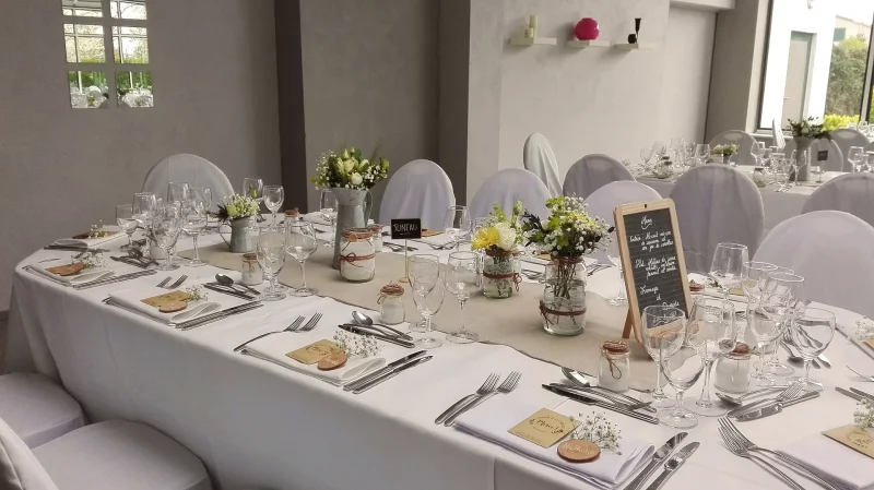 Rustic table centrepieces for a wedding, featuring white roses, yellow craspedia and gypsophila in decorated jars.