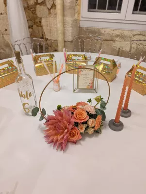 Centre de table mariage bohème avec roses pêche, dahlias, eucalyptus, et un élégant cercle doré.