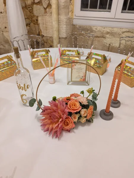Centre de table mariage bohème avec roses pêche, dahlias, eucalyptus, et un élégant cercle doré.