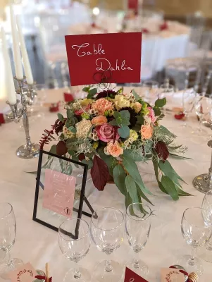 Centre de table de mariage champêtre avec roses, dahlias bordeaux, œillets pêches et feuillage d'eucalyptus, ambiance automnale.