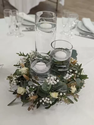 Arrangement floral de centre de table bohème avec roses blanches, eucalyptus, gypsophile et bougies flottantes.