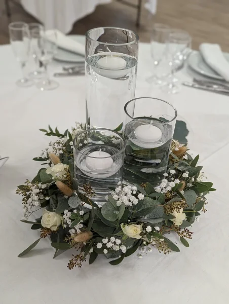 Arrangement floral de centre de table bohème avec roses blanches, eucalyptus, gypsophile et bougies flottantes.