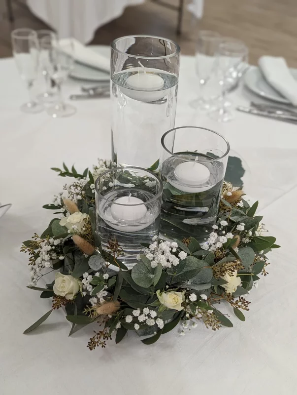 Arrangement floral de centre de table bohème avec roses blanches, eucalyptus, gypsophile et bougies flottantes.