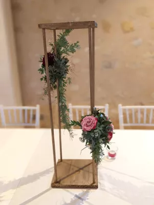Centre de table champêtre avec roses roses et bordeaux, eucalyptus et fougères sur structure bois pour mariage.