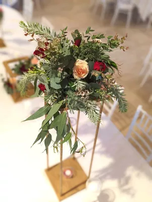 Composition florale champêtre avec roses pêche et bordeaux, eucalyptus et feuillage sur structure bois haute.