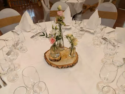 A rustic wedding table centrepiece featuring white and blush roses, eucalyptus, and a wooden log slice. A spring-inspired floral design.