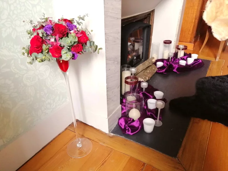 Centre de table haut pour mariage, avec des roses rouges, eucalyptus et fleurs pourpres, dans un vase élancé.