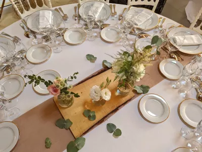 Centre de table rond champêtre avec roses, eustoma et feuillage d'eucalyptus dans des vases sur un chemin de table en bois.