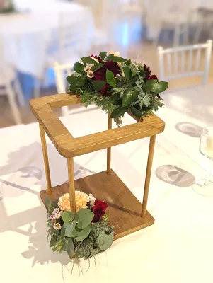 Centre de table bohème avec roses bordeaux et pêche, feuillage luxuriant sur une structure bois basse, pour mariage.