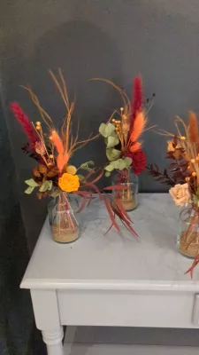 Small sophisticated rustic table centrepieces with orange roses, dried flowers, and autumn foliage.