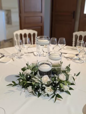 Centre de table élégant pour mariage, avec des roses blanches, du gypsophile et des bougies flottantes, créant une ambiance romantique.