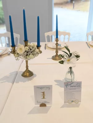 Wedding table centrepiece with white roses, gypsophila, orchid, blue candles, and gold candelabra.