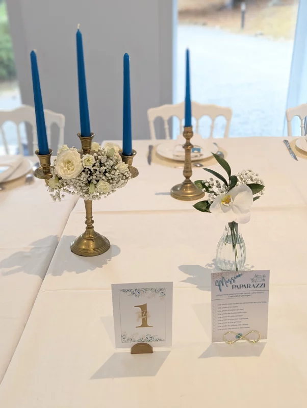 Wedding table centrepiece with white roses, gypsophila, orchid, blue candles, and gold candelabra.