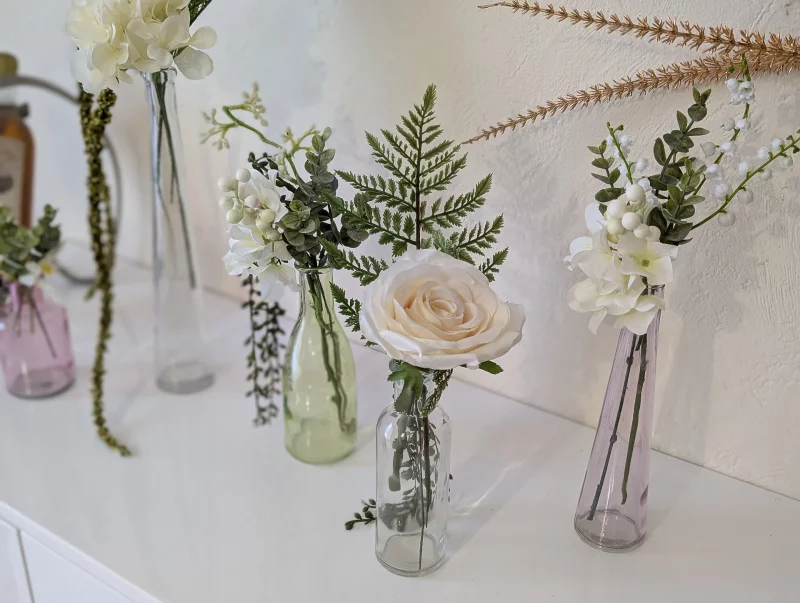 Centre de table élégant et classique pour mariage d'hiver avec roses blanches, hortensias et feuillage vert dans des vases en verre.