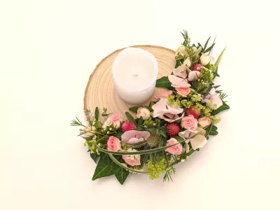 Décoration de centre de table champêtre avec roses, lisianthus, chardons et feuillage sur une base en bois brut.