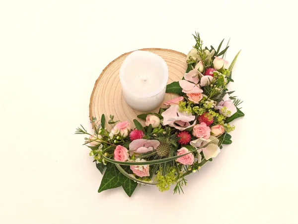 Décoration de centre de table champêtre avec roses, lisianthus, chardons et feuillage sur une base en bois brut.