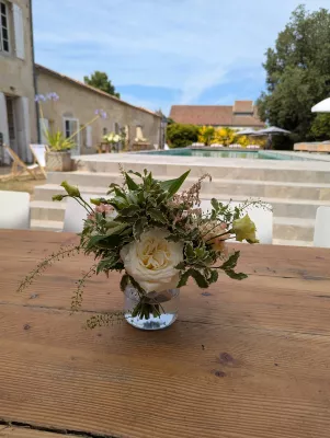 Centre de table champêtre pour mariage, avec rose crème, lisianthus pâle et feuillage varié sur table en bois.