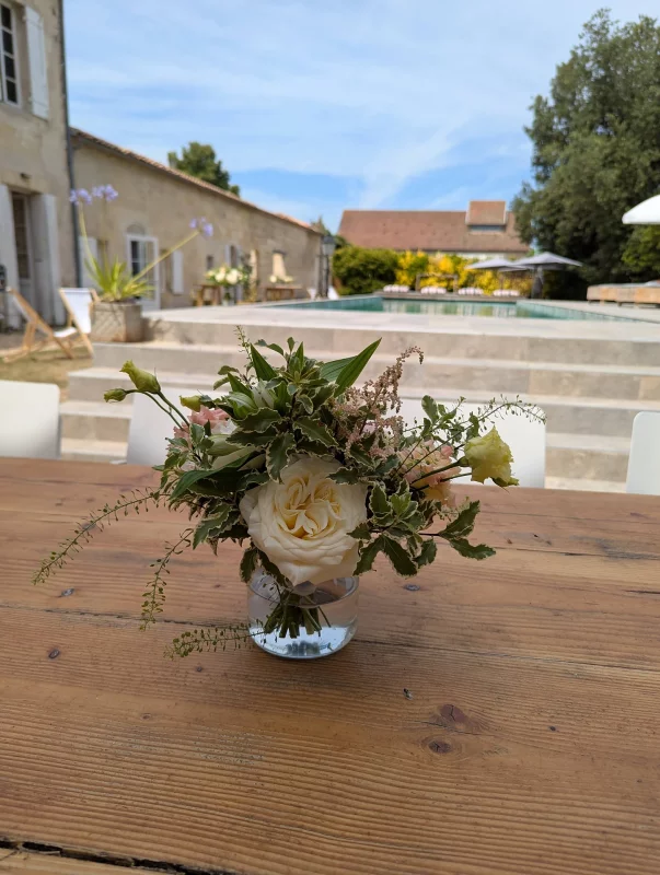 Centre de table champêtre pour mariage, avec rose crème, lisianthus pâle et feuillage varié sur table en bois.