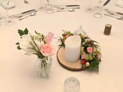 Centre de table champêtre avec roses poudrées, lisianthus blancs, gypsophile et feuillage vert sur tranche de bois.