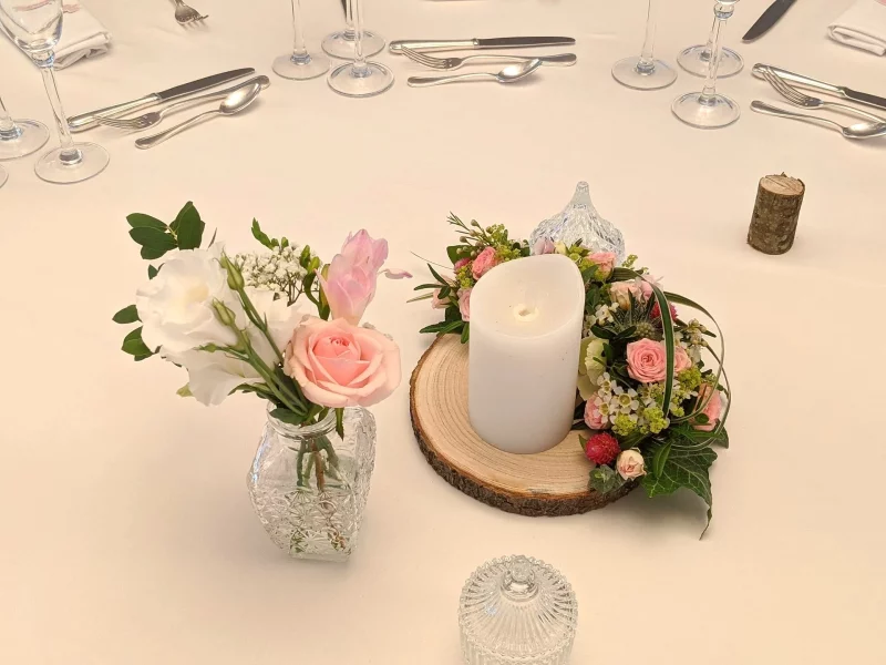 Rustic Table Centrepiece featuring dusty pink roses, white lisianthus, gypsophila and green foliage on a wooden slice.