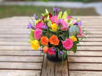Centre de table champêtre coloré pour un mariage, avec des roses vives, lisianthus et feuillage d'eucalyptus, posé sur une table en bois.