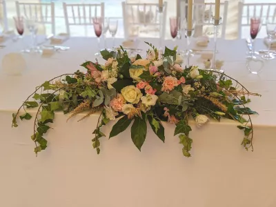 Décoration florale de table d'honneur avec roses crème, roses pâles, œillets et lisianthus, agrémentée de lierre.