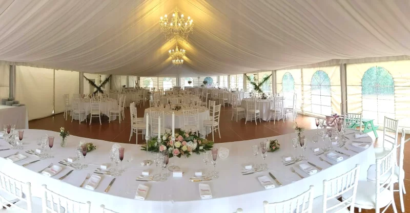 Panoramic view of a wedding reception venue featuring a classic table centrepiece of roses, lisianthus, and foliage.