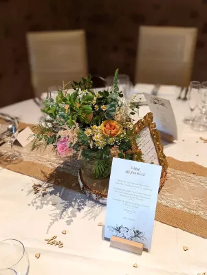 Centre de table bohème pour mariage avec rose pêche, marguerites et feuillage dense, posé sur rondin de bois.