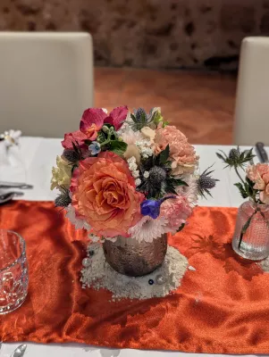 Sophisticated rustic table centrepiece with orange roses, pink carnations, and blue thistles.