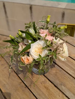 Centre de table champêtre avec rose crème, pivoine blanche, alstroemeria pêche et feuillage varié pour mariage.