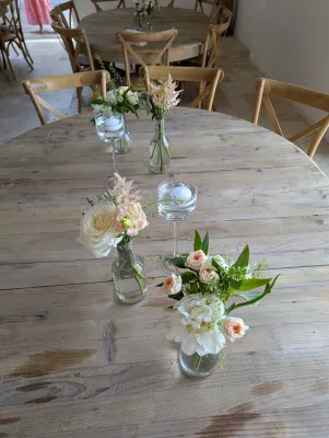 Centre de table champêtre pour mariage, avec roses crème, pivoine blanche et astilbe rose, sur table en bois rustique.