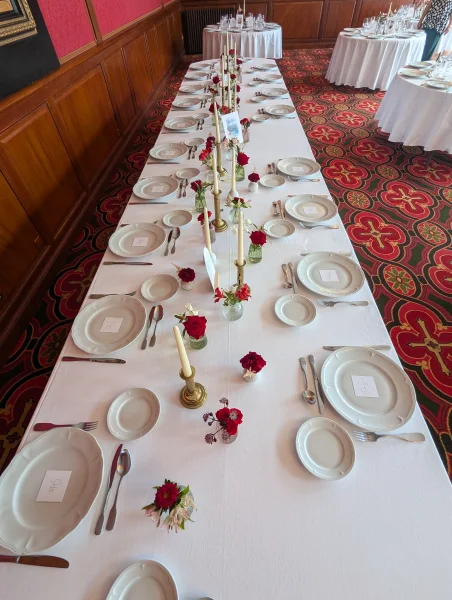 Longue table d'honneur classique pour un mariage, décorée de roses rouges, petits arrangements et bougies dorées.