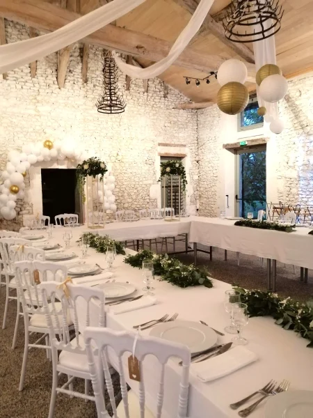 Grande salle de mariage champêtre avec tables décorées de guirlandes florales, roses blanches, eucalyptus et gypsophile pour une ambiance élégante et naturelle.