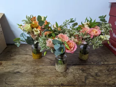 Petits centres de table bohèmes en vases, roses pêche, alstroemeria rose et eucalyptus, décor mariage estival.