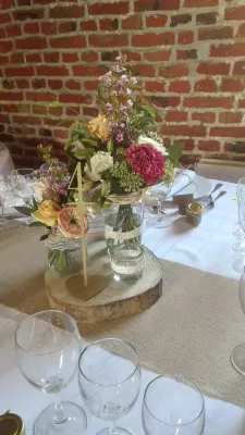 Centre de table mariage bohème-champêtre avec œillets bordeaux, roses pêche, sur un rondin de bois.