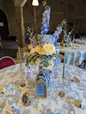 Décoration de centre de table classique avec vase bleu et blanc, roses crème et delphiniums bleus pour un mariage.