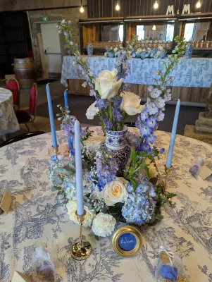 Centre de table classique de mariage avec hortensias bleus, roses crème, et delphiniums dans un vase en céramique.